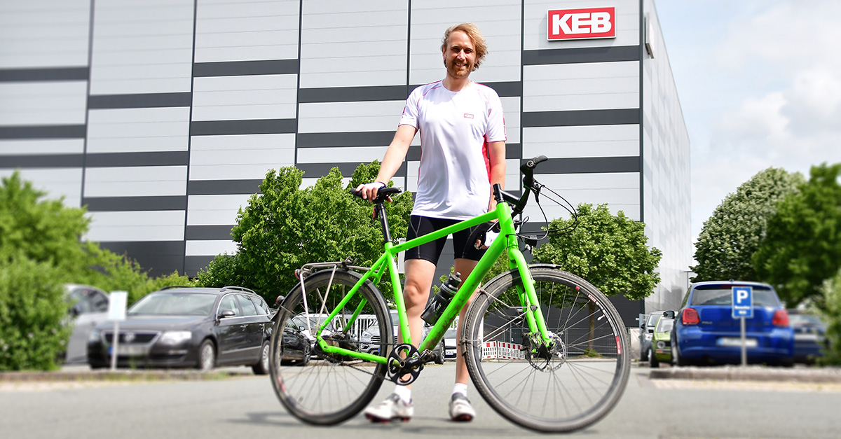 A man with a bicycle in front of a KEB building